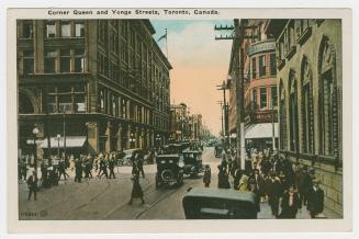 Picture of a street intersection with stores, streetcars and people walking. 