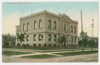 Picture of two storey library building with small trees and lawn out front. 