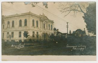 Photograph of street with library building in forefront and other buildings in background. 