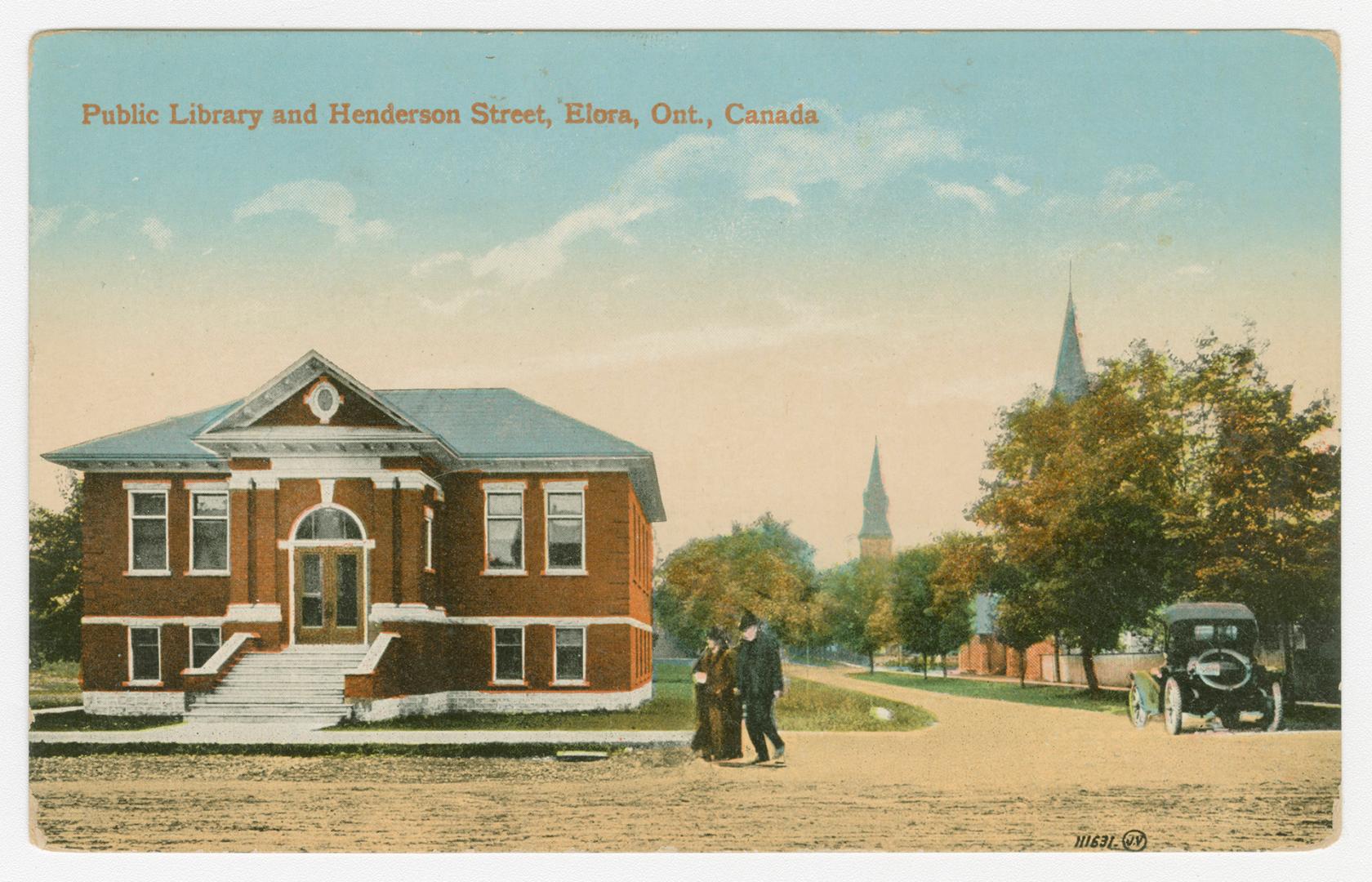 Picture of street corner with library on left and trees and church towers on right. 