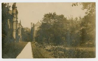 Sepia-toned postcard depicting a photo of the exterior and pathway beside Trinity College. The …