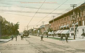 Picture of a wide street with buildings on one side, trees on other. Streetcar coming down the …