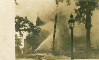 Black and white photograph of a fire pumpers dousing flames on a huge Richardsonian Romanesque …