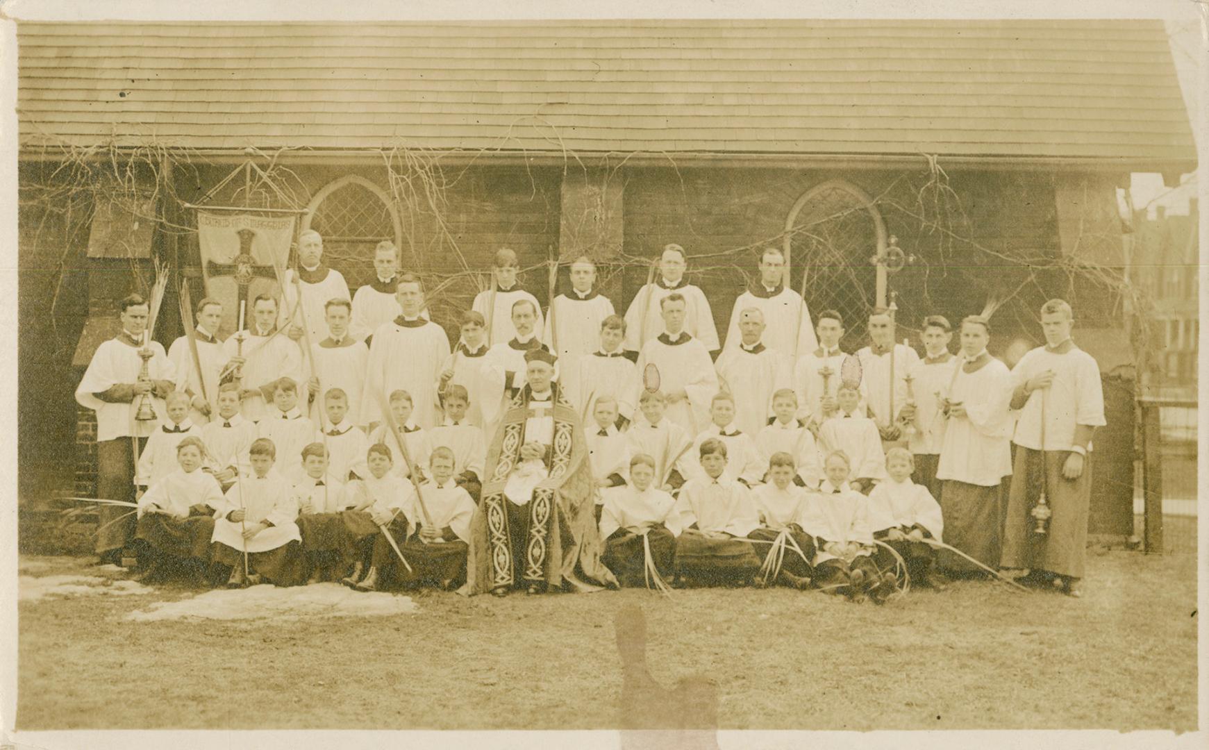 Sepia-toned postcard depicting a group photo of the Minister, church staff, and altar boys/choi…