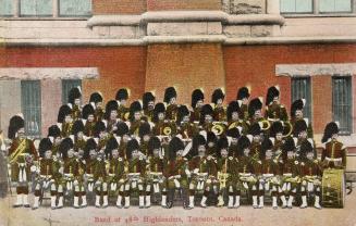 Colorized photograph of a large marching band in Scottish dress posing in front of a castle-lik…