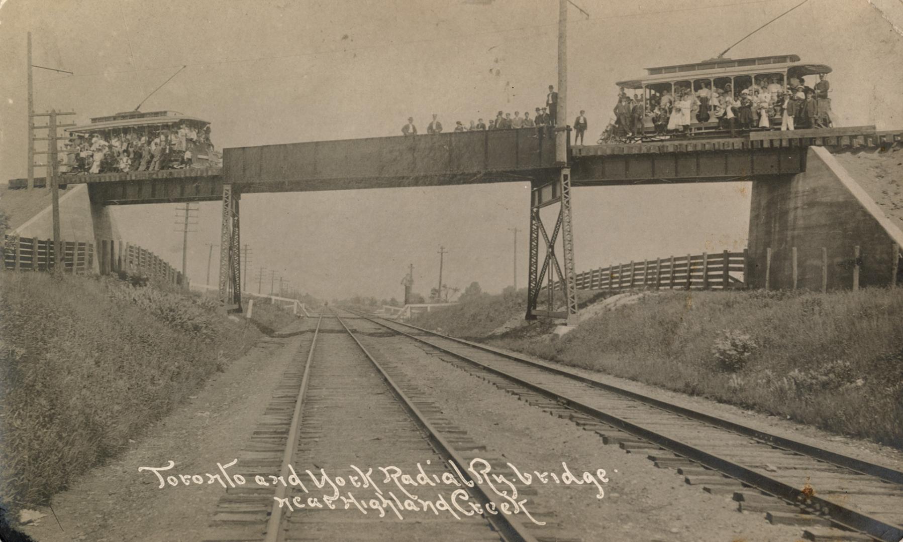 Picture of two open streetcars filled with people crossing a bridge. 