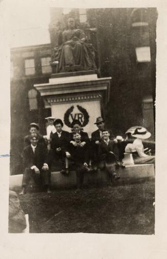 Picture of group of people sitting at the base of Queen Victoria monument. 