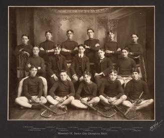 A photograph of a lacrosse team, with sixteen young men sitting and standing in a studio facing…