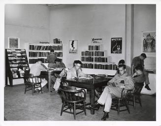 Photo of men reading at tables in a library. 