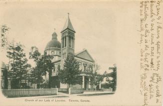 Black and white photograph of a city street bordered by large houses, trees and a big church.