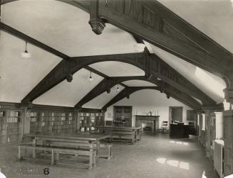 Photo of large library room with wooden arched ceiling and wooden tables, fireplace built in sh…