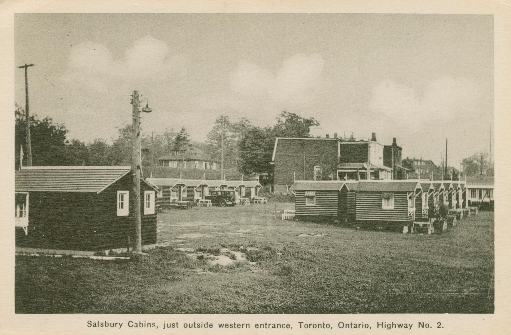 Black and white photograph of a rows of small, frame cabins on a field of grass.