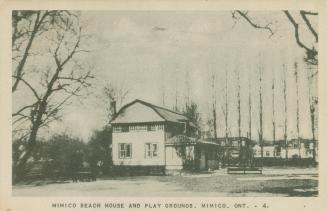 Black and white photograph of a two story house on a beach with park benches in front of it.