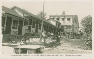 Black and white photograph of a row of summer cottages in front of a larger house.