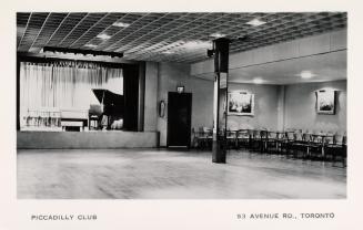 Black and white photo postcard depicting a large room with chairs off to the side and a grand p…