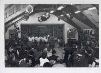 Photo of crowd seated and watching group of women singers and band. 