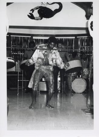 Photo of limbo dancer with steel band in background. 