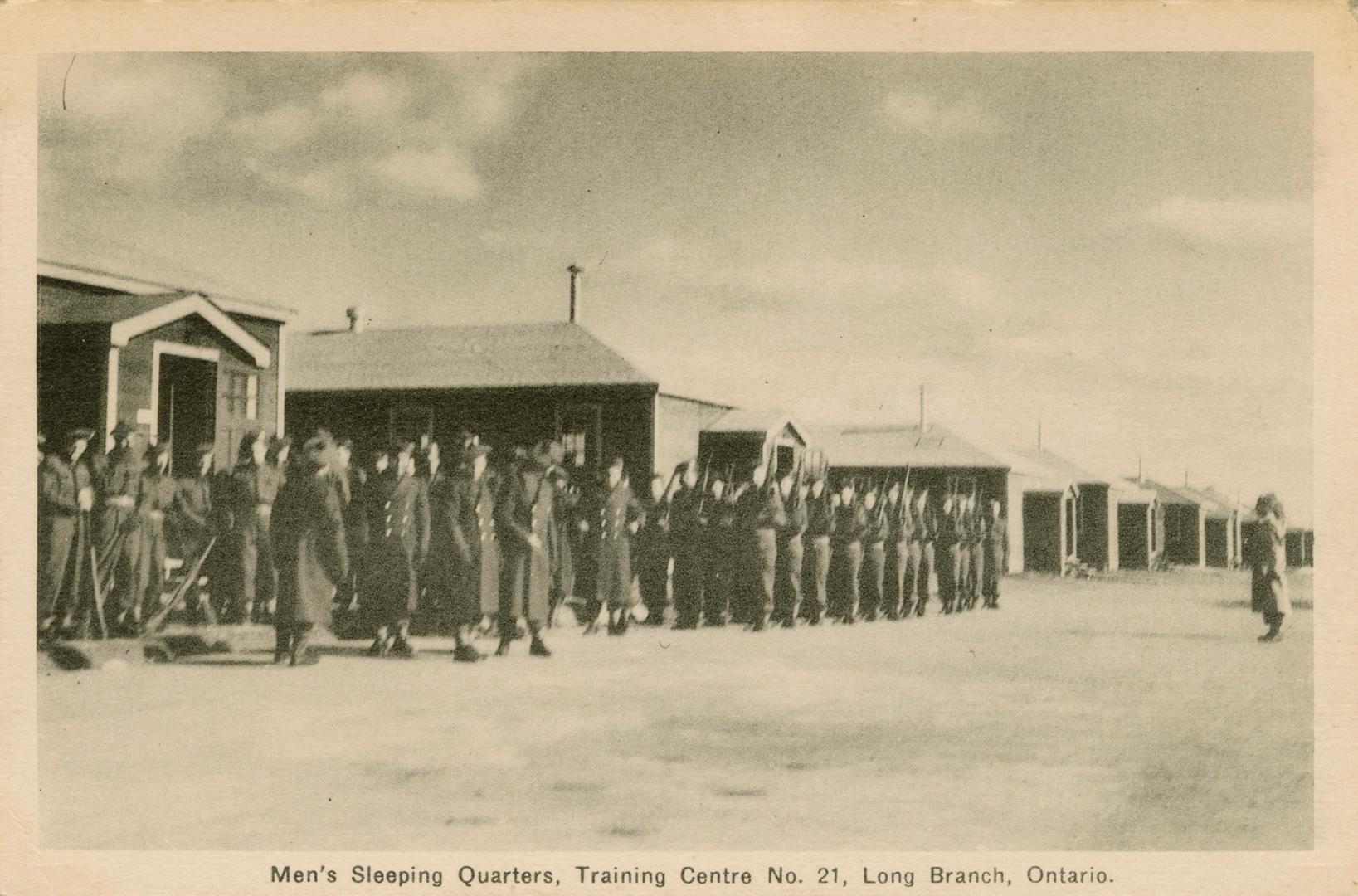 Sepia-toned photo postcard depicting men lined up in front of the sleeping quarters at a Canadi…