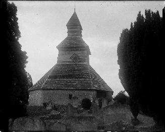 A photograph of a belfry, with a clock on the side facing the photographer. There are graveston…