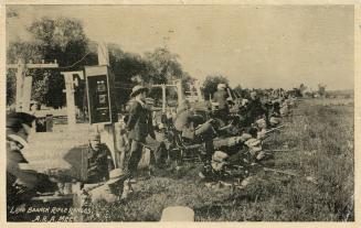 Sepia-toned photo postcard depicting men aiming their rifles outwards at an outdoor rifle range…