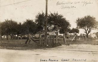 Sepia-toned photo postcard depicting a camping facility with streetcar tracks running across th…