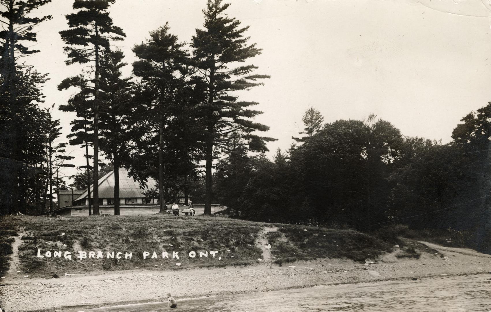 Black/white photo postcard depicting a beach and clubhouse with caption at the bottom stating, …