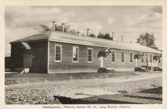 Sepia-toned photo postcard depicting a bungalow with several doors, at a Canadian Army Training…