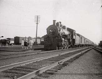 A photograph of a rail yard, with a stationary train pointed towards the photographer on one se…