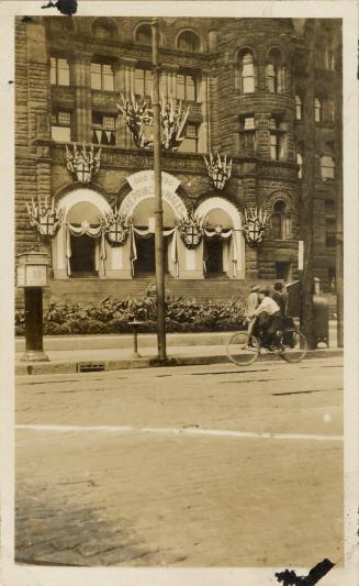 A photograph of a building decorating with bunting and flags. There is a sidewalk in front of t…