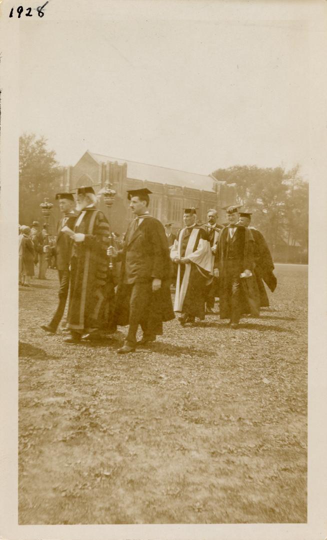 A photograph of a group of people wearing academic robes and mortarboards walking across a gras…