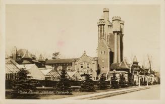 Black and white picture of a castle with greenhouses in front of it.