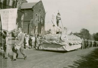 A photograph of a parade through a university campus, with people in suits and ties walking on …