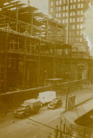 A photograph of a large building under construction, with metal beams exposed. There is a paved…