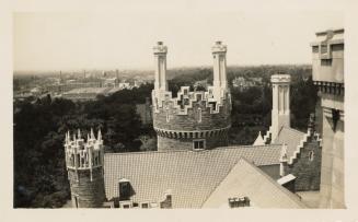 A photograph of a stone castle-like building, taken from a high vantage point on top of part of…