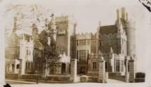 A photograph of a stone castle-like building, with round towers, spires, gates and ledges and l…