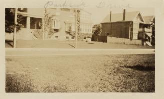 A photograph of a residential city street, with houses on the far side of the road and a grass  ...