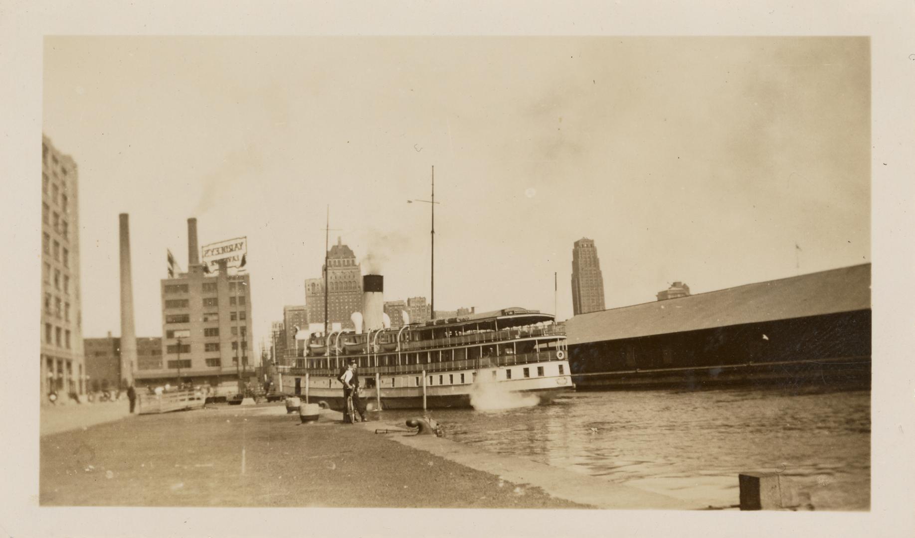 A photograph of a city harbour, with a ferry docked by a concrete pier and tall office building…