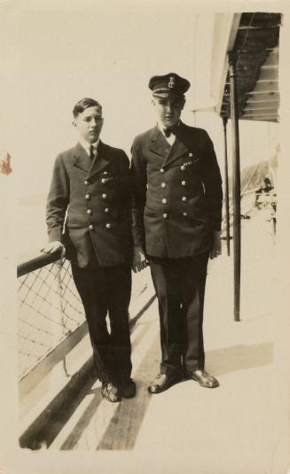 A photograph of two people standing on the deck of a ferry and wearing uniforms with two rows o…