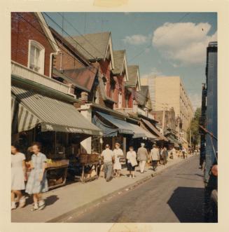 A photograph of a city street, with two and three story buildings on the left side of the road  ...