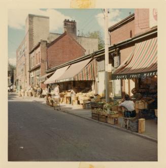 A photograph of a city street, with two and three story buildings on the right side of the road ...