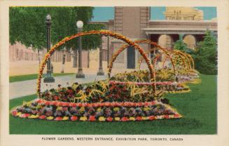 Colorized photograph of people standing in front of a large gate entrance composed of two tower…