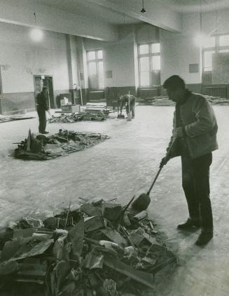 A photograph of three workers with brooms and dustpans cleaning up an interior space. There are…