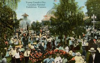 Colorized photograph of a very large crowd milling around a park with a very large, marble foun…