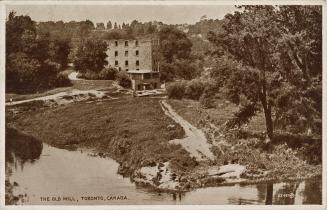 Black and whie photograph of the ruins of a five story stone building behind a narrow river.