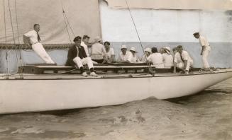 Black and white photograph of a party on a yacht against a painted backdrop.