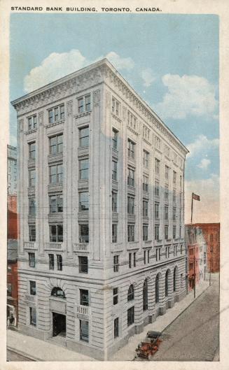 Colorized photograph of an eight story skyscraper building taken from a corner angle. A car is …