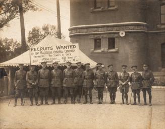 A photograph of a military recruiting tent in front of a large brick or stone building, located…