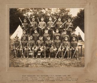 A photograph of a group of twenty men in military uniforms posing for a photograph in a grass f…