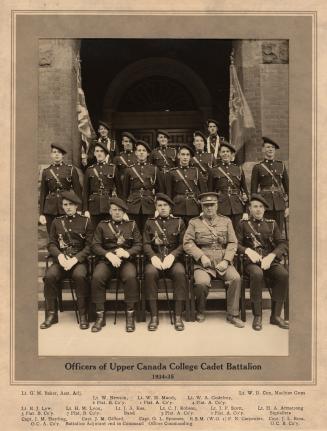 A photograph of sixteen men posing for a photograph in front of the entranceway to a large ston…