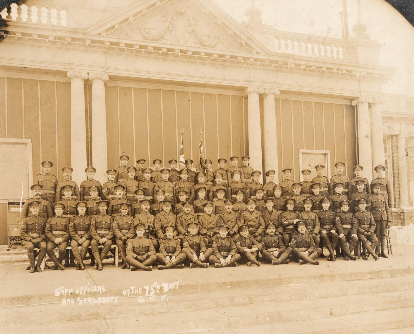 A photograph of a large group of people posing in front of a one-story stone building in a Beau…